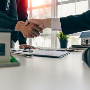 Two business professionals shaking hands over a desk in office setting, symbolizing an successful deal