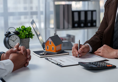 Two people signing documents on a desk with a small house and clock, for Title Services & Refinancing Support in Broward County